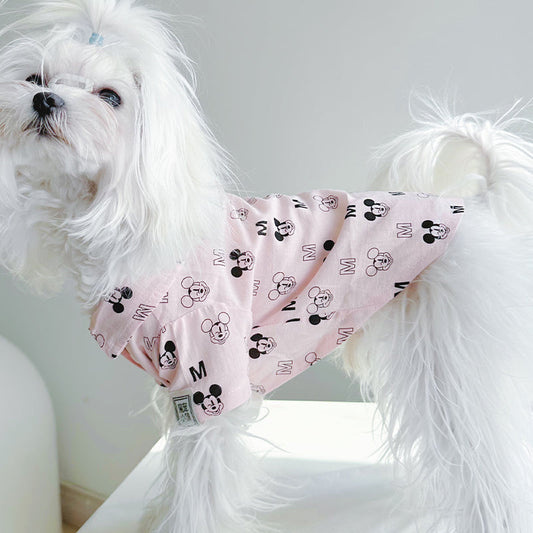 White fluffy dog wearing a pink short-sleeve graphic dog shirt with a classic collar