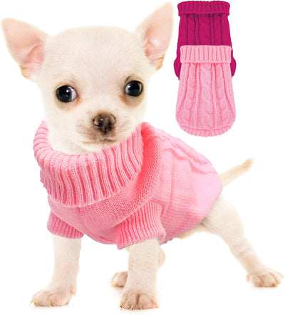 Tiny white Chihuahua wearing a light pink cable knit turtleneck sweater beside matching pink and rose dog sweaters.